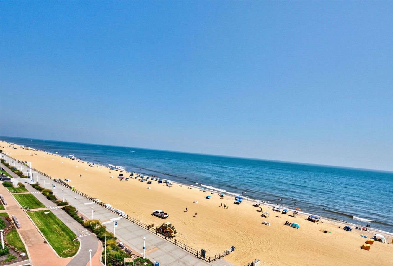 A beach with a paved walkway and a clear view of the ocean.