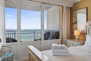 A hotel room with a bed, a chair, a nightstand, a lamp, and a view of the ocean. - New / Beachfront Condo/ Pool/ Surfing/ EW 801 (Virginia Beach)