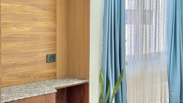 A room with a wooden desk, a potted plant, and a window with blue curtains.