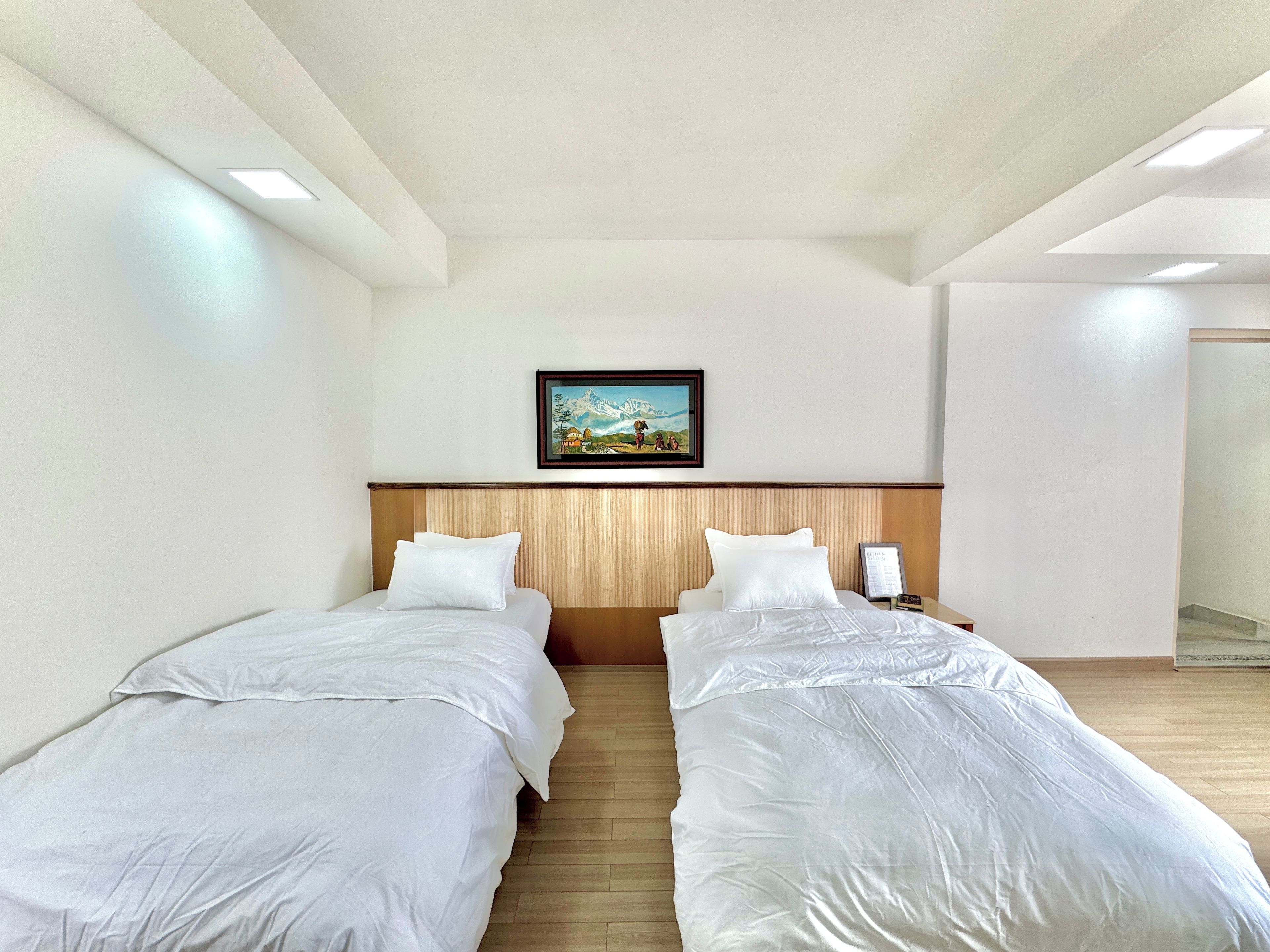 A hotel room with two beds, a wooden headboard, a painting on the wall, and a nightstand with a lamp.