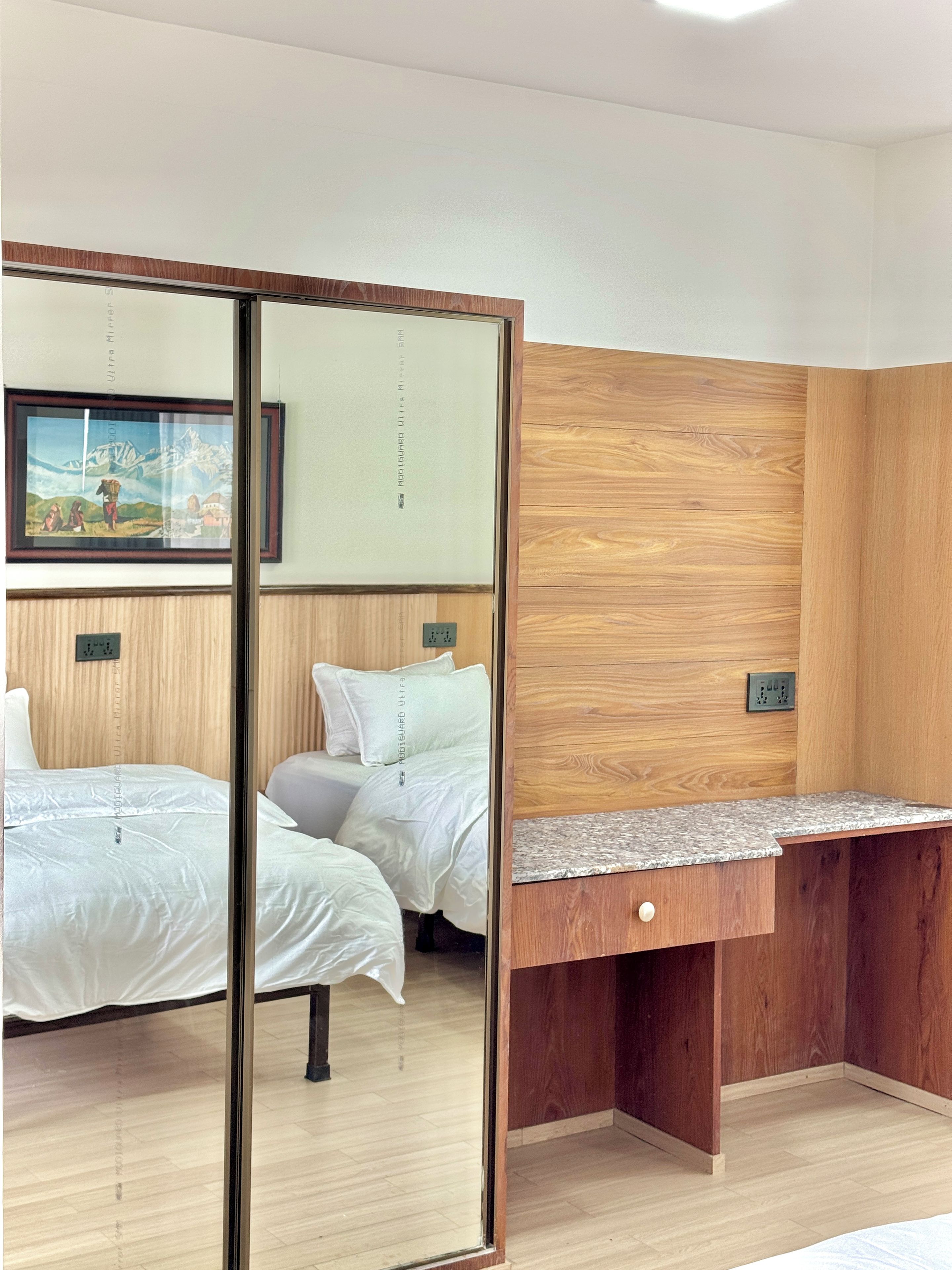Quarto de hotel com parede de painel de madeira, cama com roupa de cama branca, mesa de cabeceira e um espelho.