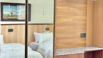 Quarto de hotel com parede de painel de madeira, cama com roupa de cama branca, mesa de cabeceira e um espelho.