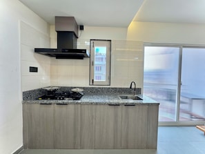 A kitchen with a built-in stove, a range hood, and a window overlooking a cityscape. - Pulukisi Residence (Kathmandu)