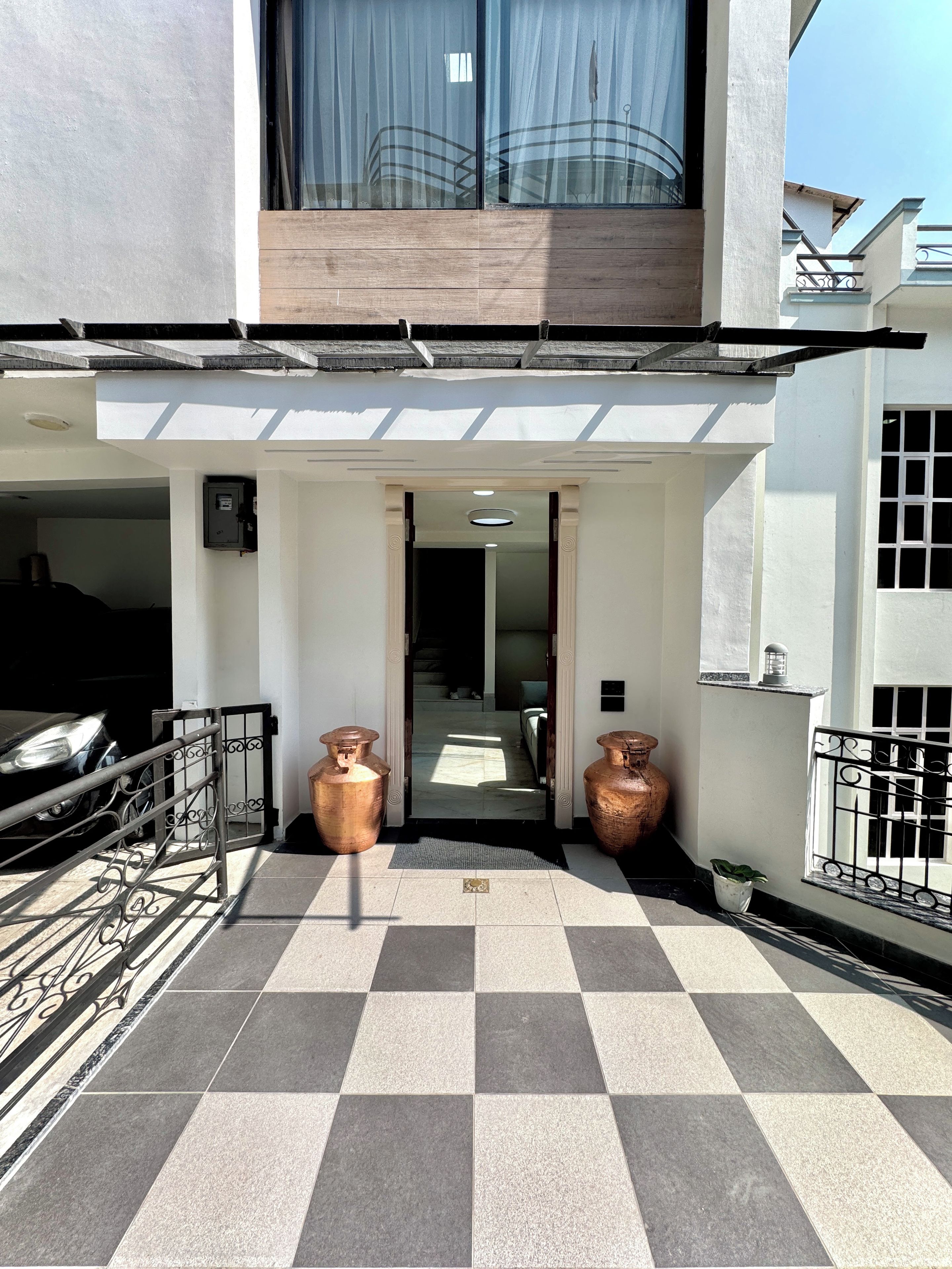 Entrada de um edifício com piso xadrez, um portão e dois vasos grandes.