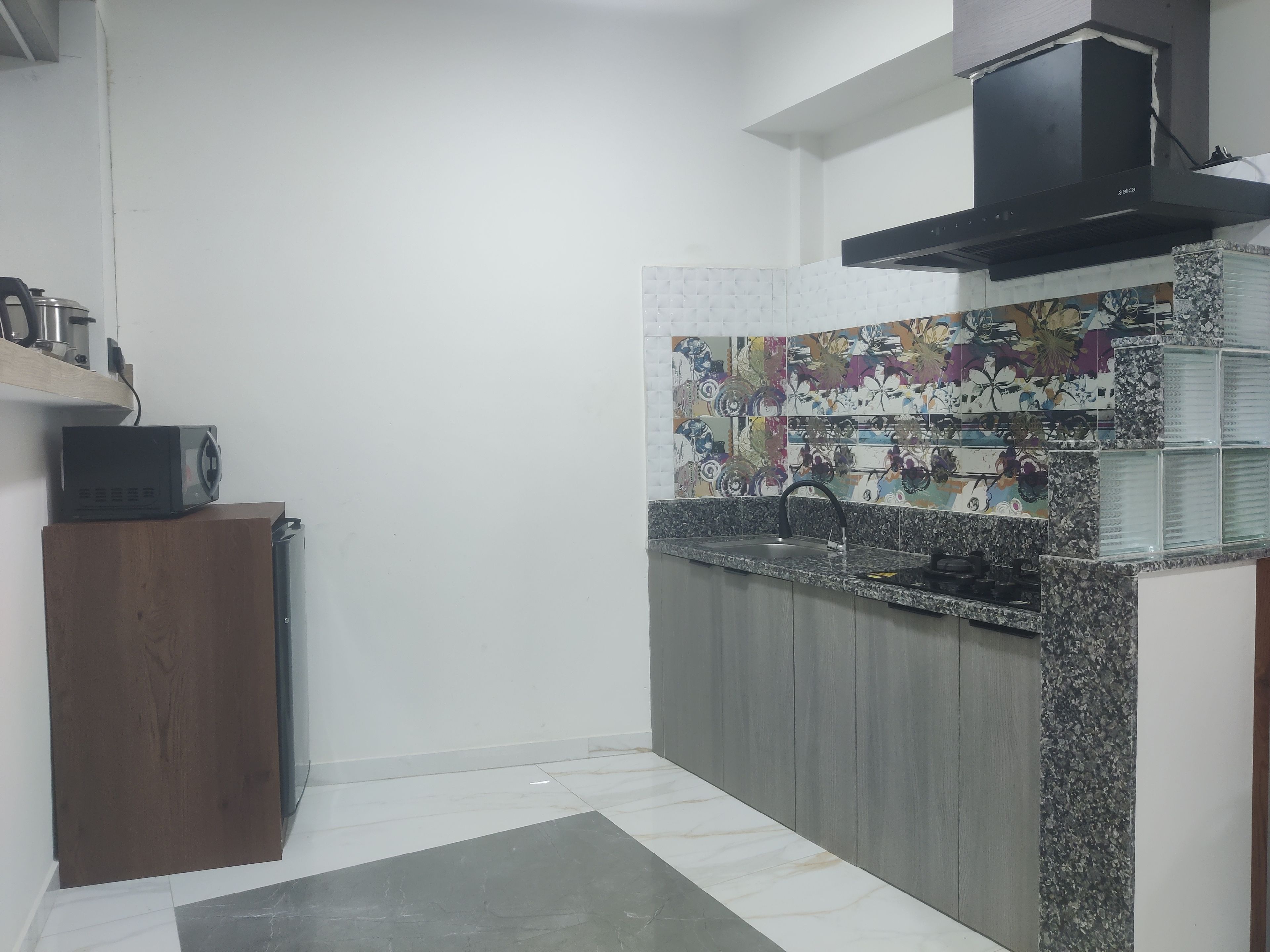 A kitchen with a microwave on a wooden cabinet, a sink with a faucet, and a decorative backsplash.