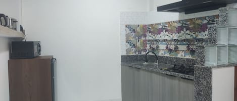 A kitchen with a microwave on a wooden cabinet, a sink with a faucet, and a decorative backsplash.