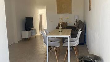 A dining area with a table and chairs, a television in the background, and a decorative vase on the table.