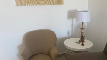 A room with a beige armchair, a small round table with a lamp, and a brown sofa.