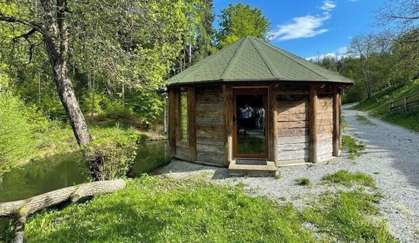 A wooden gazebo with a green roof, situated beside a gravel path and a body of water, surrounded by trees. - Holiday Home in Schiefling am See With Wi-fi (Schiefling am See)