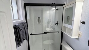 A compact bathroom with a glass-enclosed shower, a white toilet, and a sink with a mirror above it. - Lovely 4-bedroom house in Flagstaff perfect for your getaway (Flagstaff)