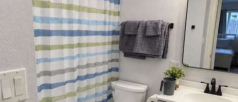 A bathroom with a striped shower curtain, a toilet, a sink with a mirror, and a trash bin.
