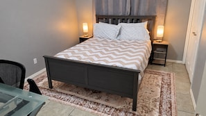 A bedroom with a bed, two bedside lamps, a chair, and a glass table.
