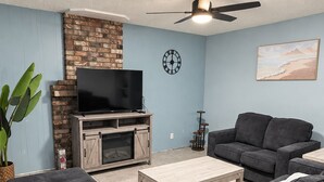 A living room with a flat-screen TV, a fireplace, a ceiling fan, and a couch.