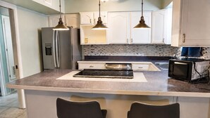 A kitchen with a large island, two pendant lights, a refrigerator, a microwave, and a tiled backsplash. - Lovely 4-bedroom house in Flagstaff perfect for your getaway (Flagstaff)