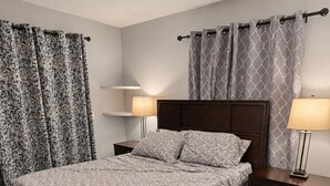 A bedroom with a bed, nightstands, lamps, a ceiling fan, patterned curtains, and a decorative rug.