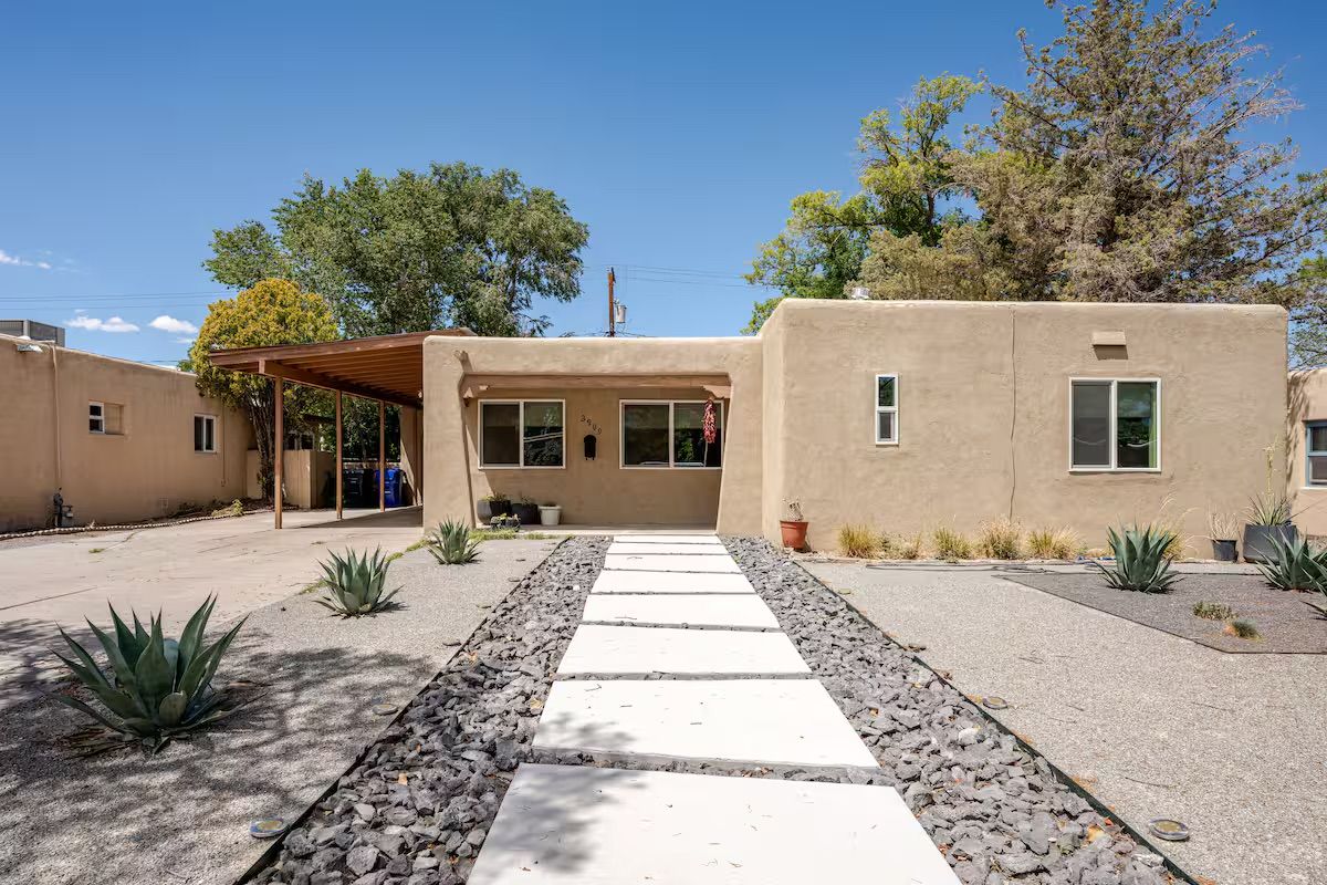 A modern building with a covered patio, a stone pathway, and desert landscaping.