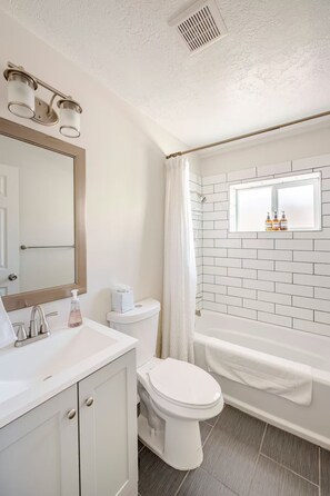 A bathroom with a toilet, sink, mirror, and shower. - Casa Serena (Albuquerque)