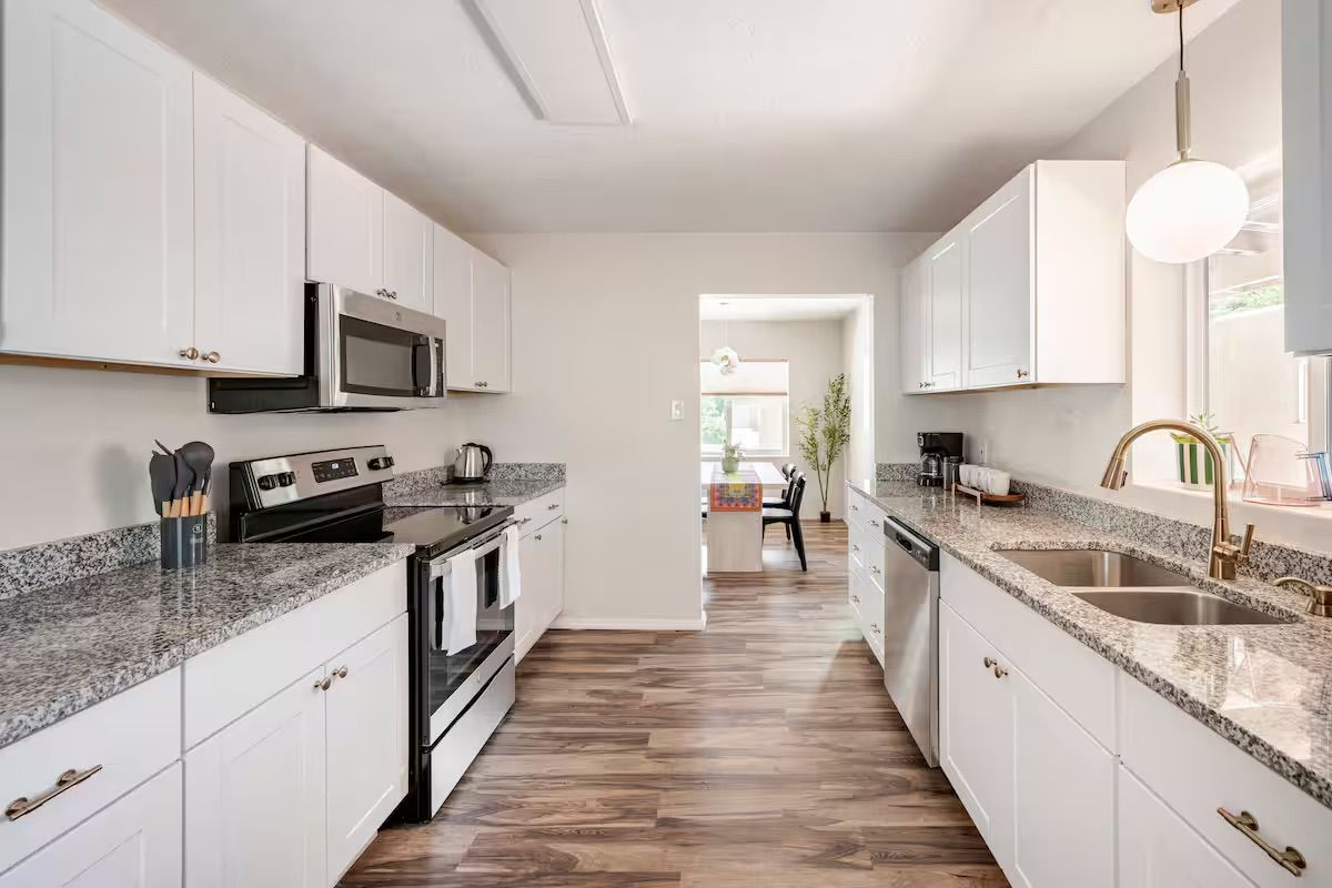 A modern kitchen with white cabinets, granite countertops, a stainless steel oven, and a large window.