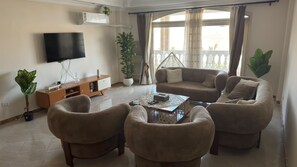 A living room with a flat-screen TV, a sofa, two armchairs, a coffee table, and a potted plant. -  3-bedroom luxury apartment with AC infront of Giza pyramids (Giza Governorate)