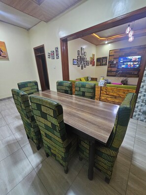 A dining area with a wooden table and patterned chairs, a green sofa, and a TV mounted on the wall.