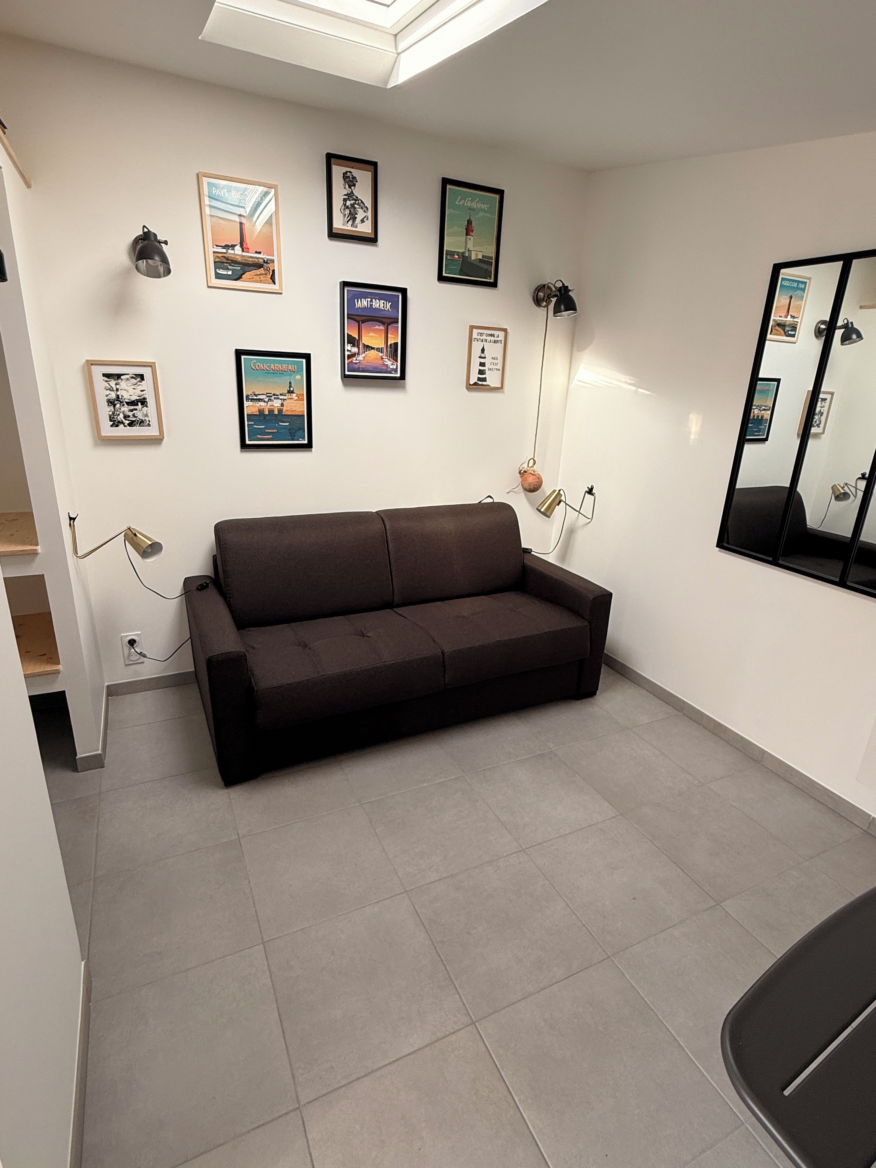 A room with a brown sofa, a large mirror, and several framed pictures on the wall.