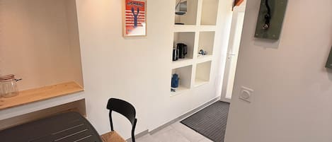 A modern interior with a dining table, chairs, a bench, a wall-mounted shelf unit, and a ceiling light fixture.
