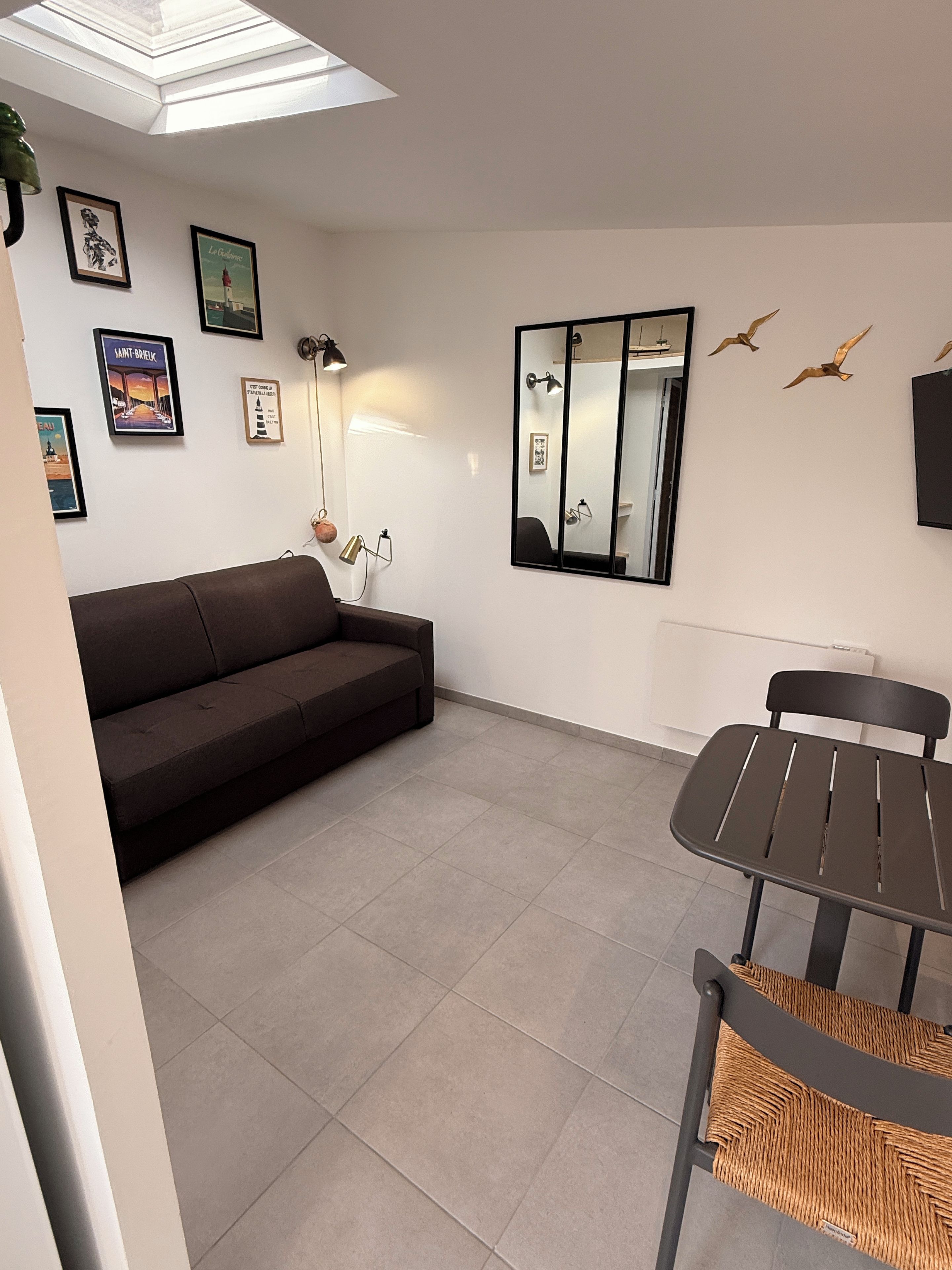 A modern living room with a sofa, a dining table with chairs, a large mirror, and wall-mounted artwork.
