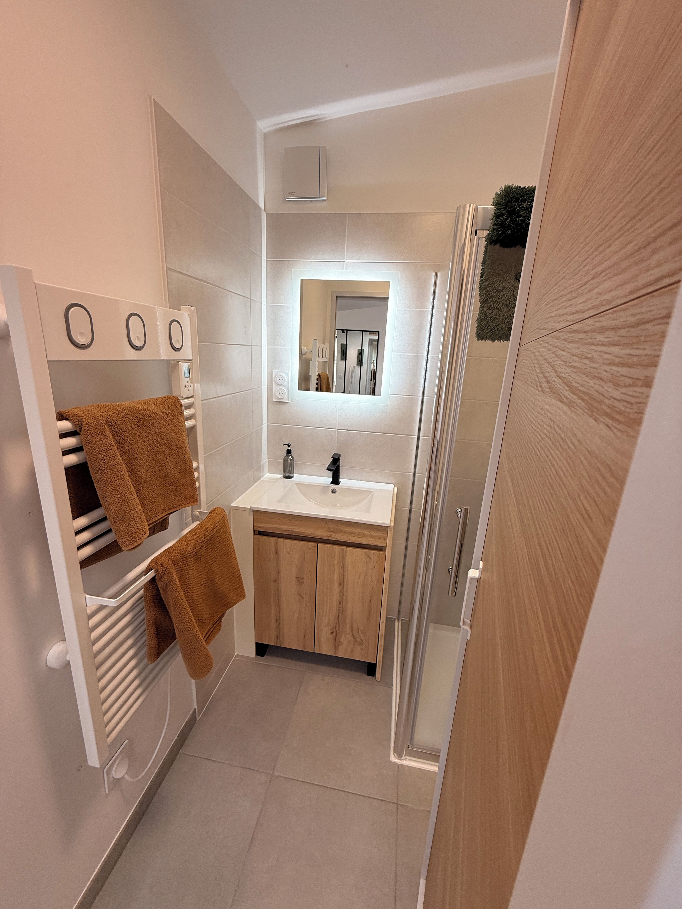 A modern bathroom with a white sink, wooden cabinets, and a glass shower enclosure.