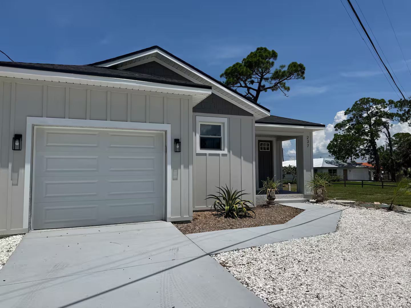 A single-story house with a garage, a small porch, and a gravel driveway.