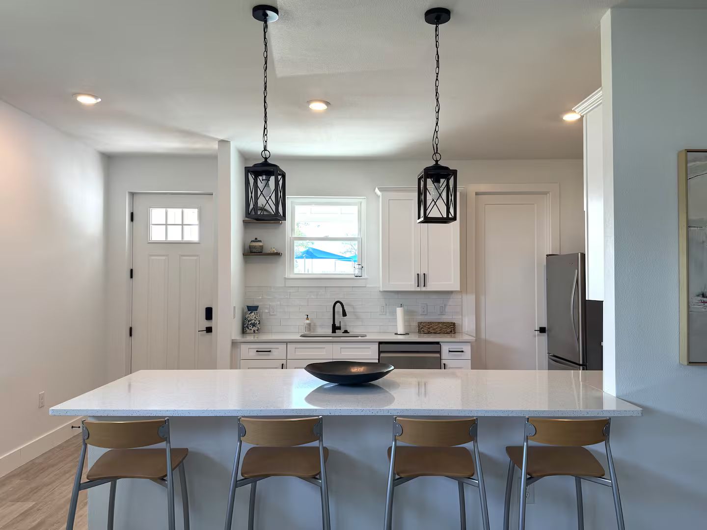 A modern kitchen with a large island, pendant lighting, and a view of the outdoors.