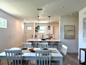 A dining area with a white table and chairs, a kitchen in the background, and a painting on the wall. - Close to Beaches ~ Downtown Venice ~ Bike Trail ~ Park (Nokomis)