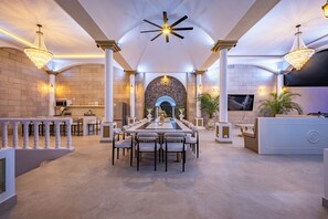 A spacious dining area with a long table, multiple chairs, and a central fireplace. - The Palace Villa Luxury Jaco Experience Olympus: Greek Gods, Jacuzzi, Pool, Bar (Jacó)
