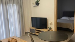 A modern living room with a TV, a dining table, and chairs. There is a bed in the adjacent room. - Villa Art Dome (Paralia)