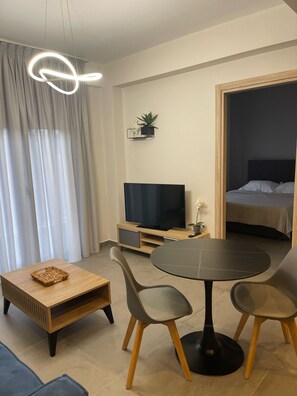 Ein modernes Wohnzimmer mit Fernseher, einem Esstisch und Stühlen. Im angrenzenden Raum befindet sich ein Bett.