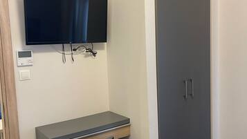 A room with a flat-screen TV mounted on the wall, a desk with a chair, and a wardrobe with two doors.