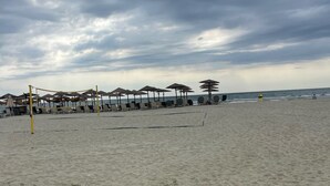 A beach with umbrellas and lounge chairs, a volleyball net, and a clear view of the ocean. - Villa Art Dome (Paralia)