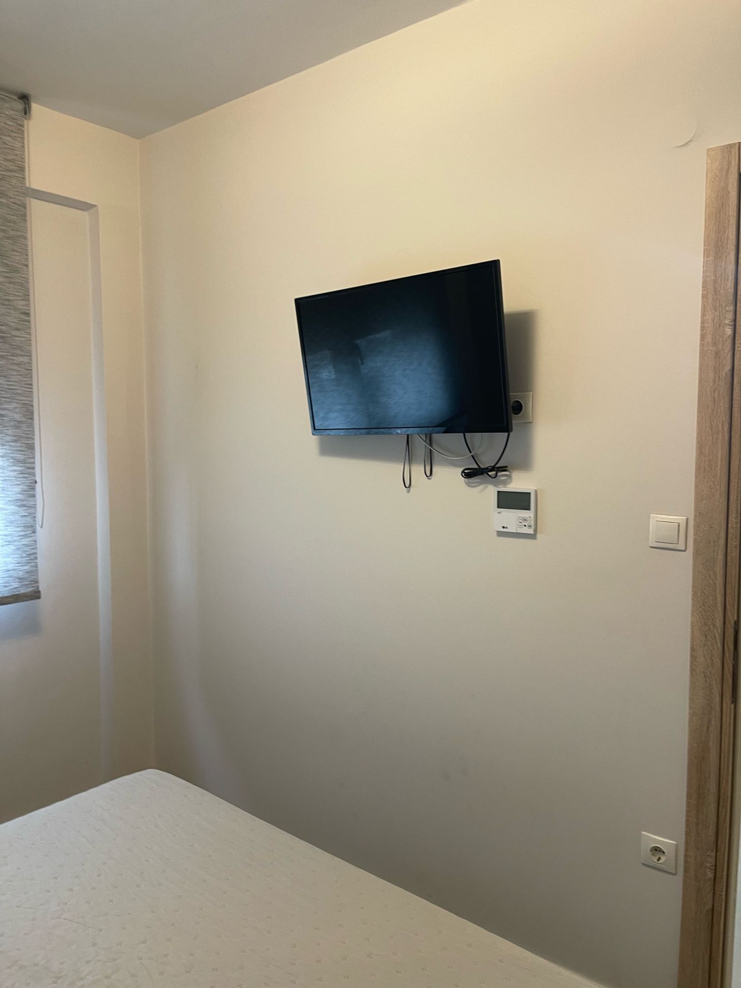 Ein Zimmer mit einem an der Wand montierten Fernseher, einem Thermostat und einer Steckdose.