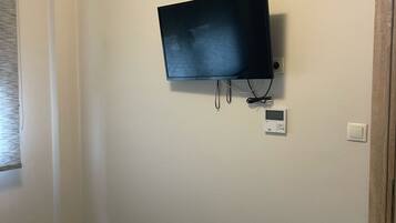 Ein Zimmer mit einem an der Wand montierten Fernseher, einem Thermostat und einer Steckdose.