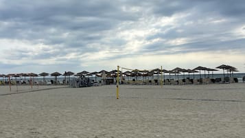 A beach with umbrellas and lounge chairs, a volleyball net, and a cloudy sky.