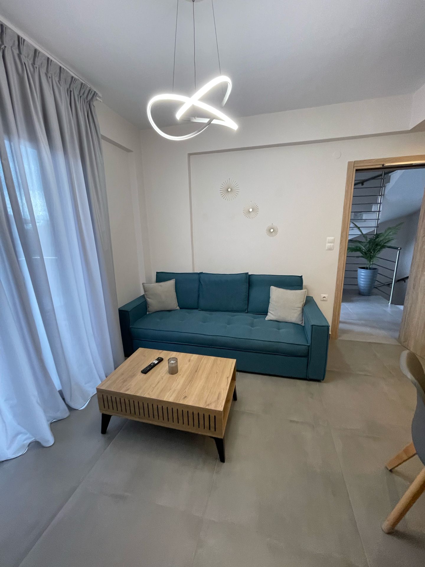 Ein modernes Wohnzimmer mit einem türkisfarbenen Sofa, einem Holztisch und einer außergewöhnlichen Deckenleuchte.