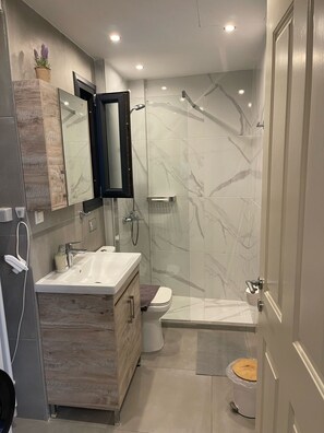 Ein modernes Badezimmer mit einer Marmerdusche, einem Waschbecken mit Spiegel und einer Toilette.