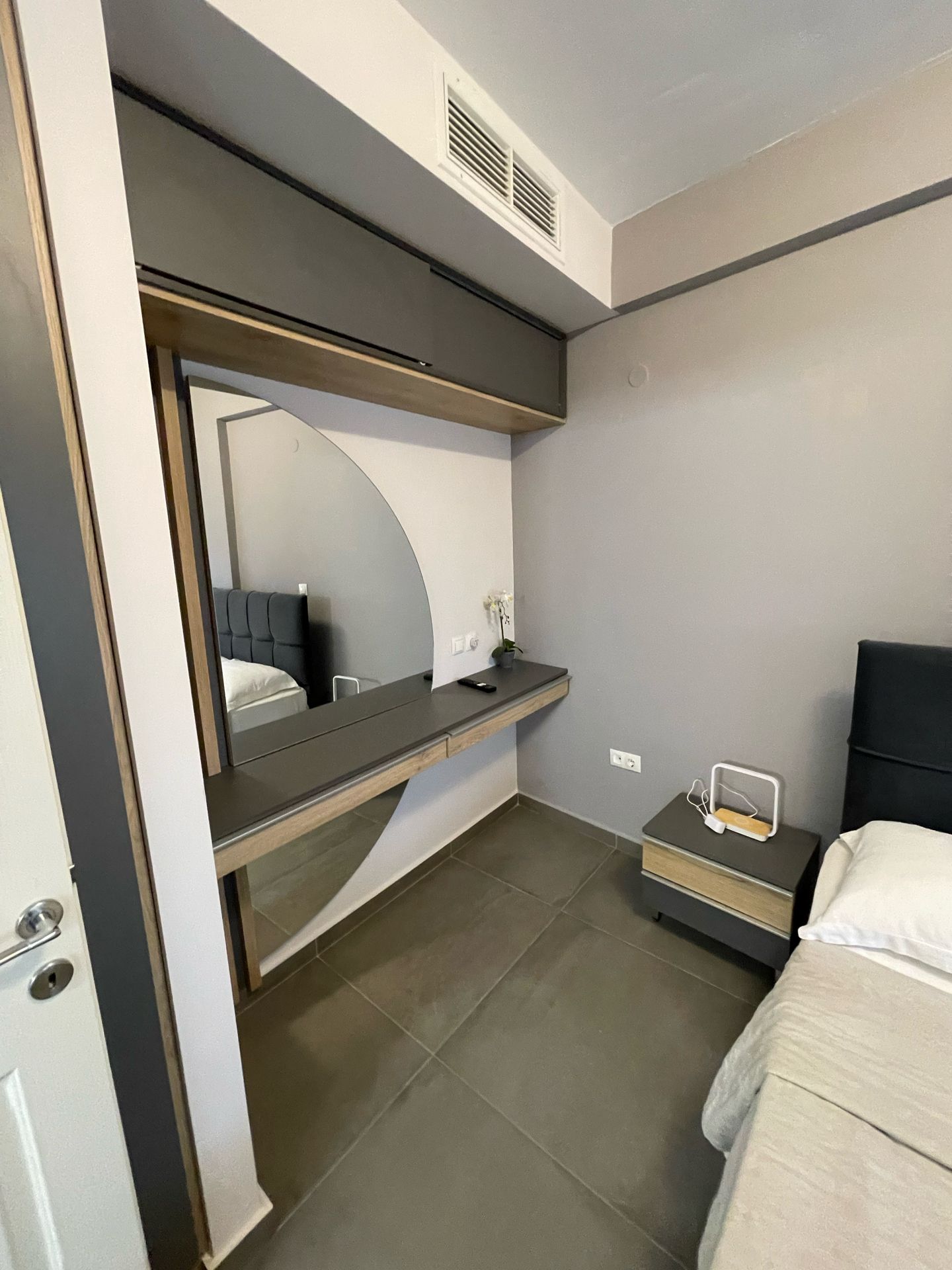 Ein modernes Hotelzimmer mit Bett, Nachttisch und integriertem Schreibtisch mit Spiegel.
