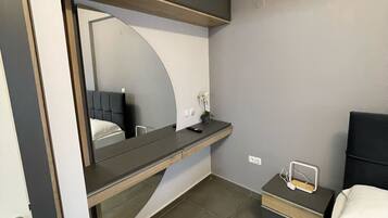Ein modernes Hotelzimmer mit Bett, Nachttisch und integriertem Schreibtisch mit Spiegel.