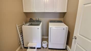 A laundry room with two white washing machines, a drying rack, and a small step stool.