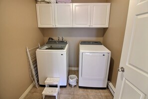 A laundry room with two white washing machines, a drying rack, and a small step stool.