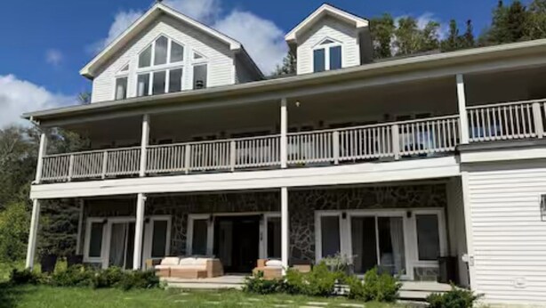 Une maison à deux étages dotée d’un balcon, d’un porche couvert et d’une façade en pierre.