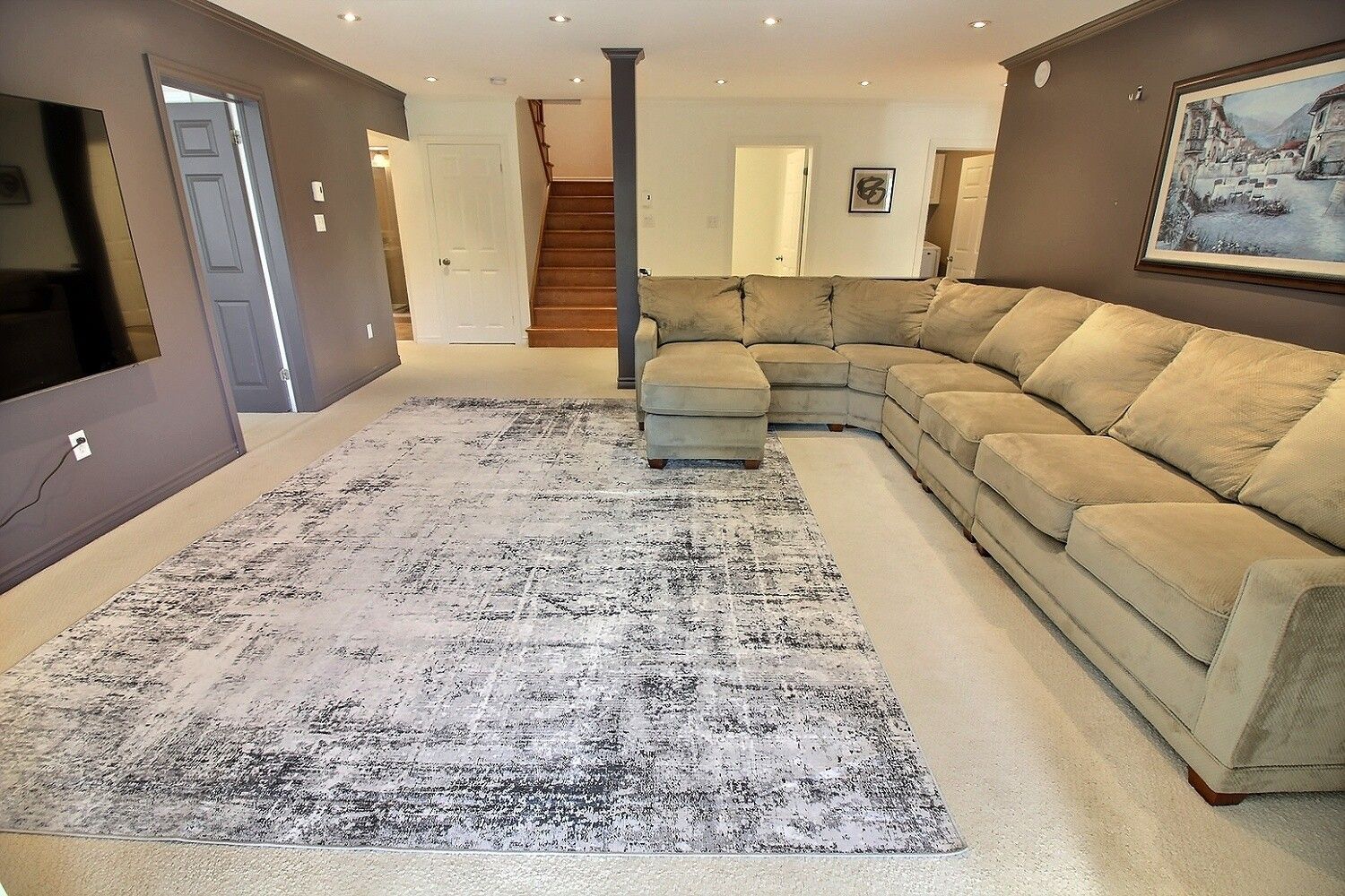 A living room with a sectional sofa, a patterned rug, and a staircase leading to another room.