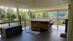 Une terrasse couverte avec un banc en bois, un jacuzzi et une vue sur un lac et une forêt.