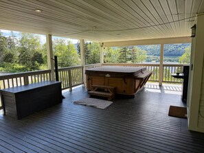 Une terrasse couverte avec un banc en bois, un jacuzzi et une vue sur un lac et une forêt.