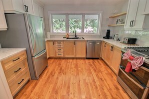 A modern kitchen with wooden cabinets, a stainless steel refrigerator, a dishwasher, and a stove.